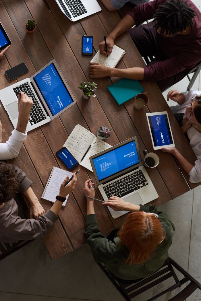 Offerings A diverse group of professionals brainstorming with laptops and notepads in a modern office.