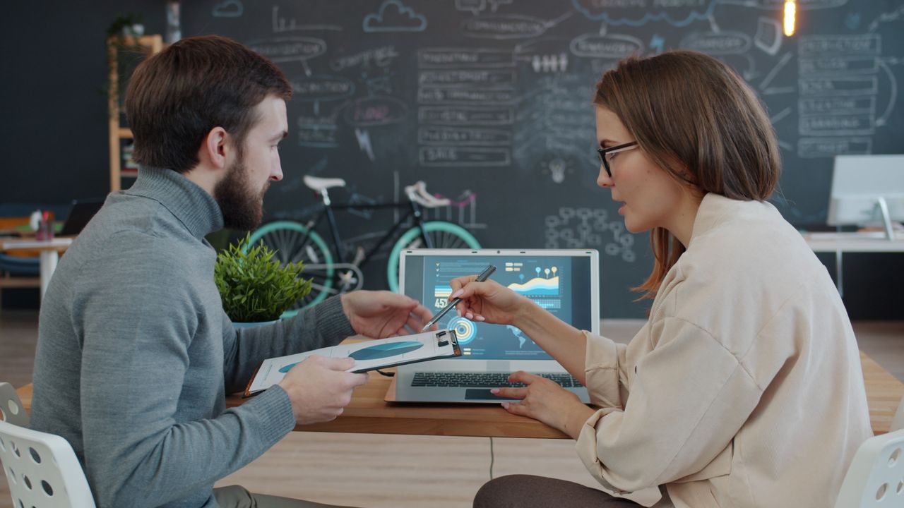 Offerings Two professionals discussing data analytics on laptop in creative office.