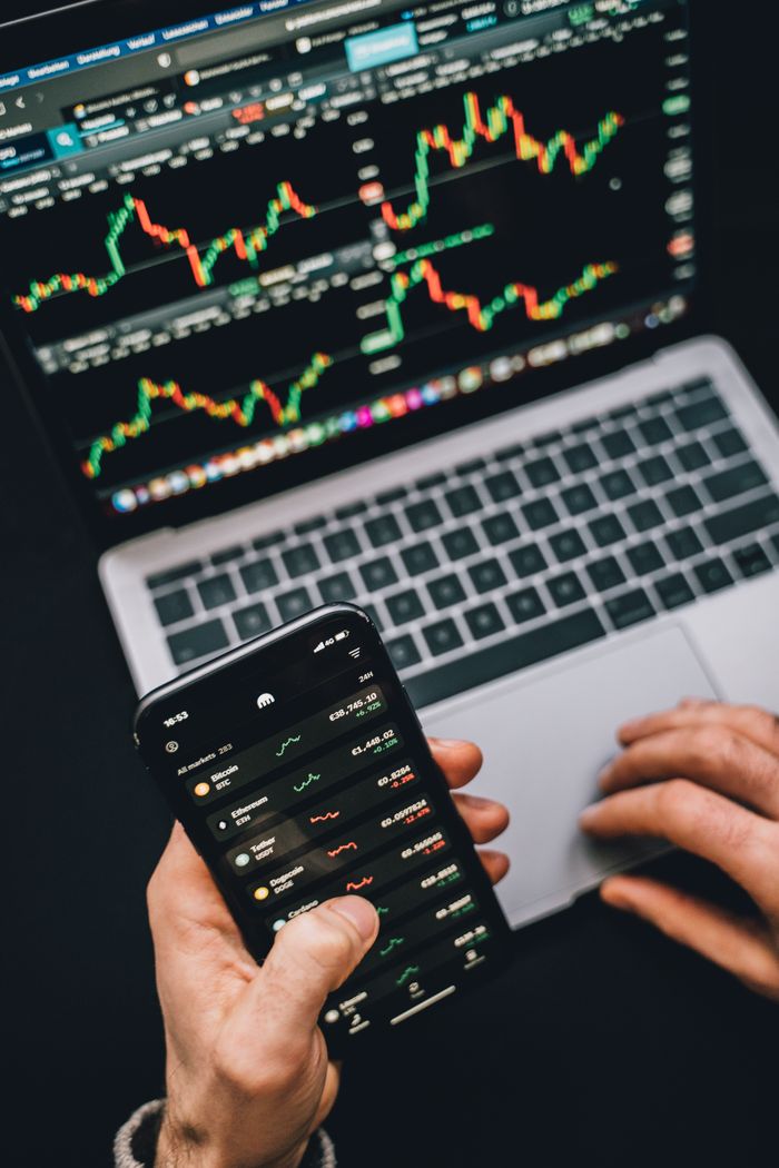 Offerings Person analyzing stock market data with a laptop and smartphone showing trading graphs.
